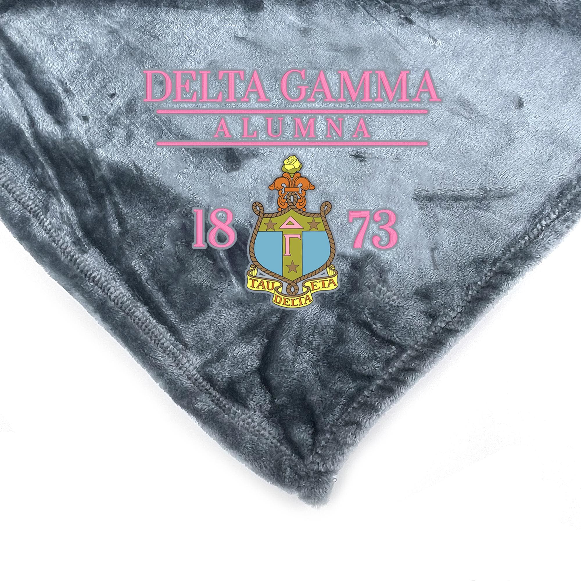 a gray fabric with the text "DELTA GAMMA ALUMNA 18 73" and a crest design, which appears to be a blanket or throw.