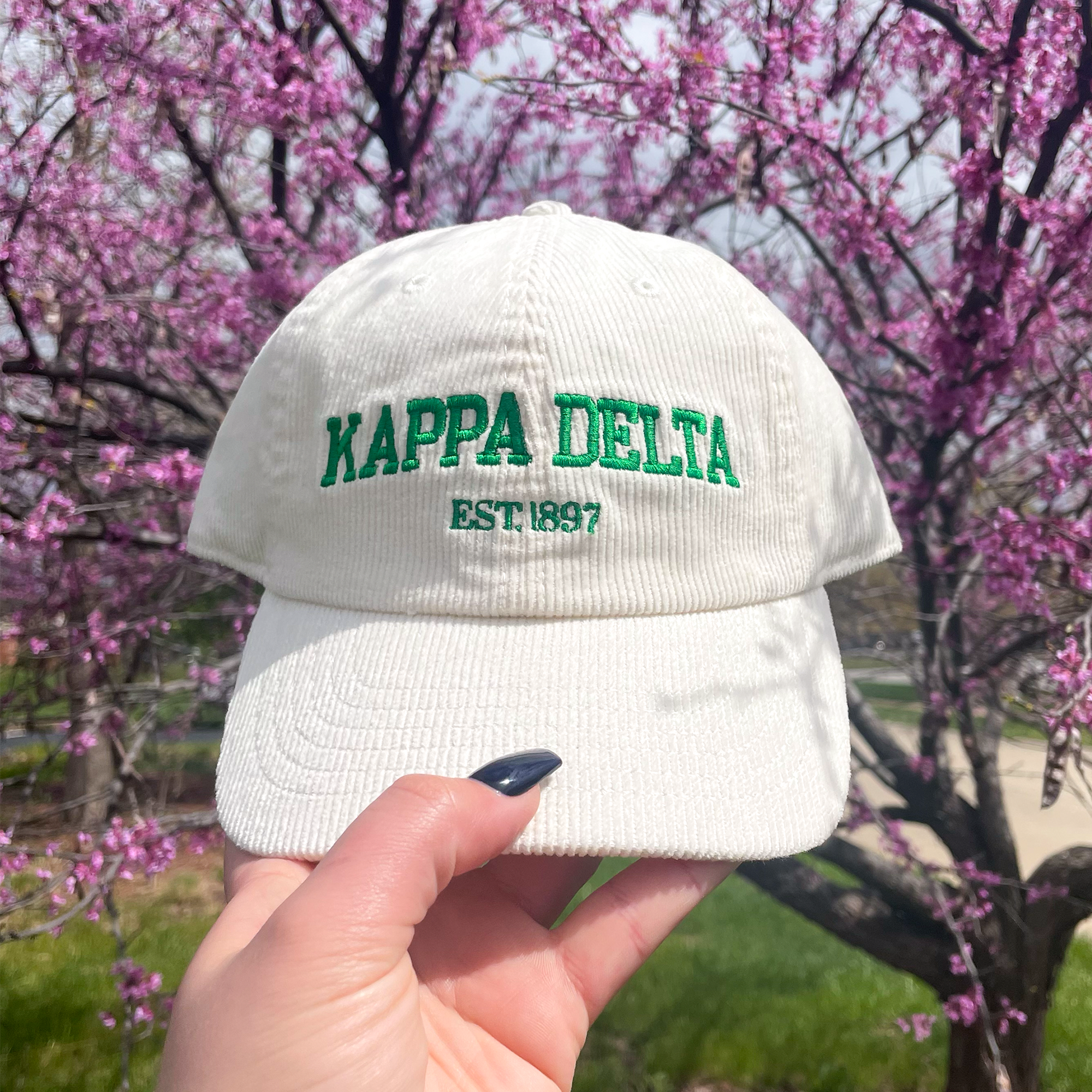 a person holding up a white hat with the words kapa delta on it