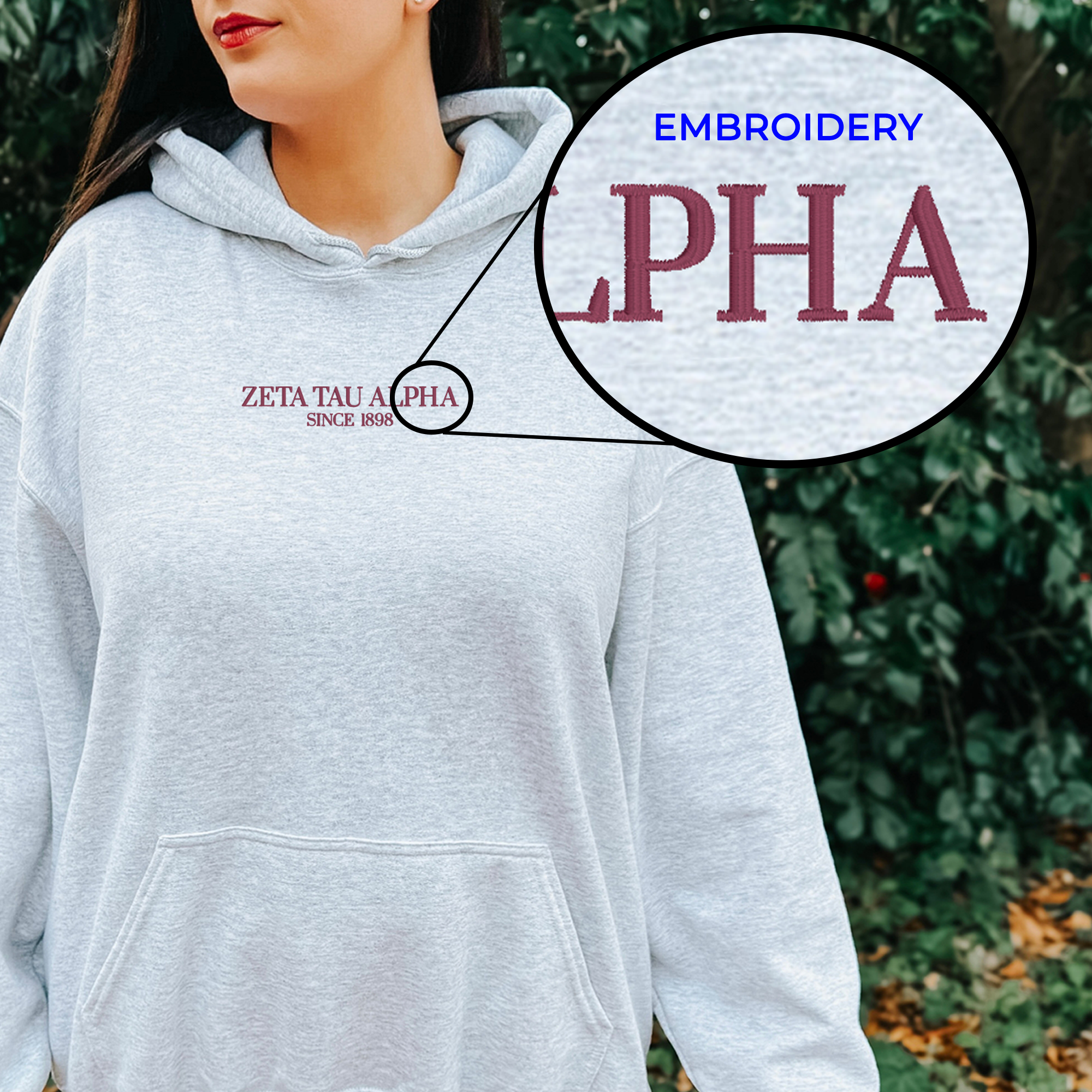 A woman wearing a grey hoodie with the embroidered text "ZETA TAU Apha Since 1898" on it, standing in front of a natural background.