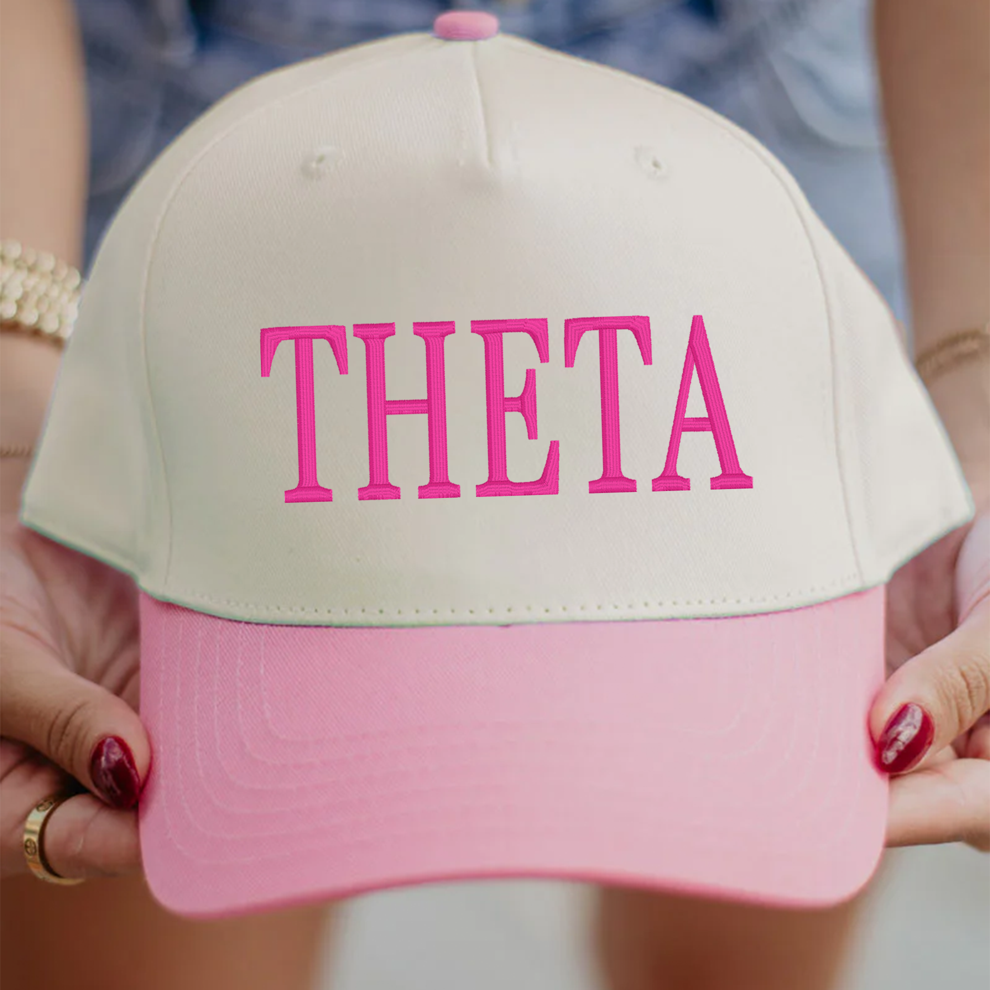 A person is holding a pink and white baseball cap with the word "THETA" printed on it.