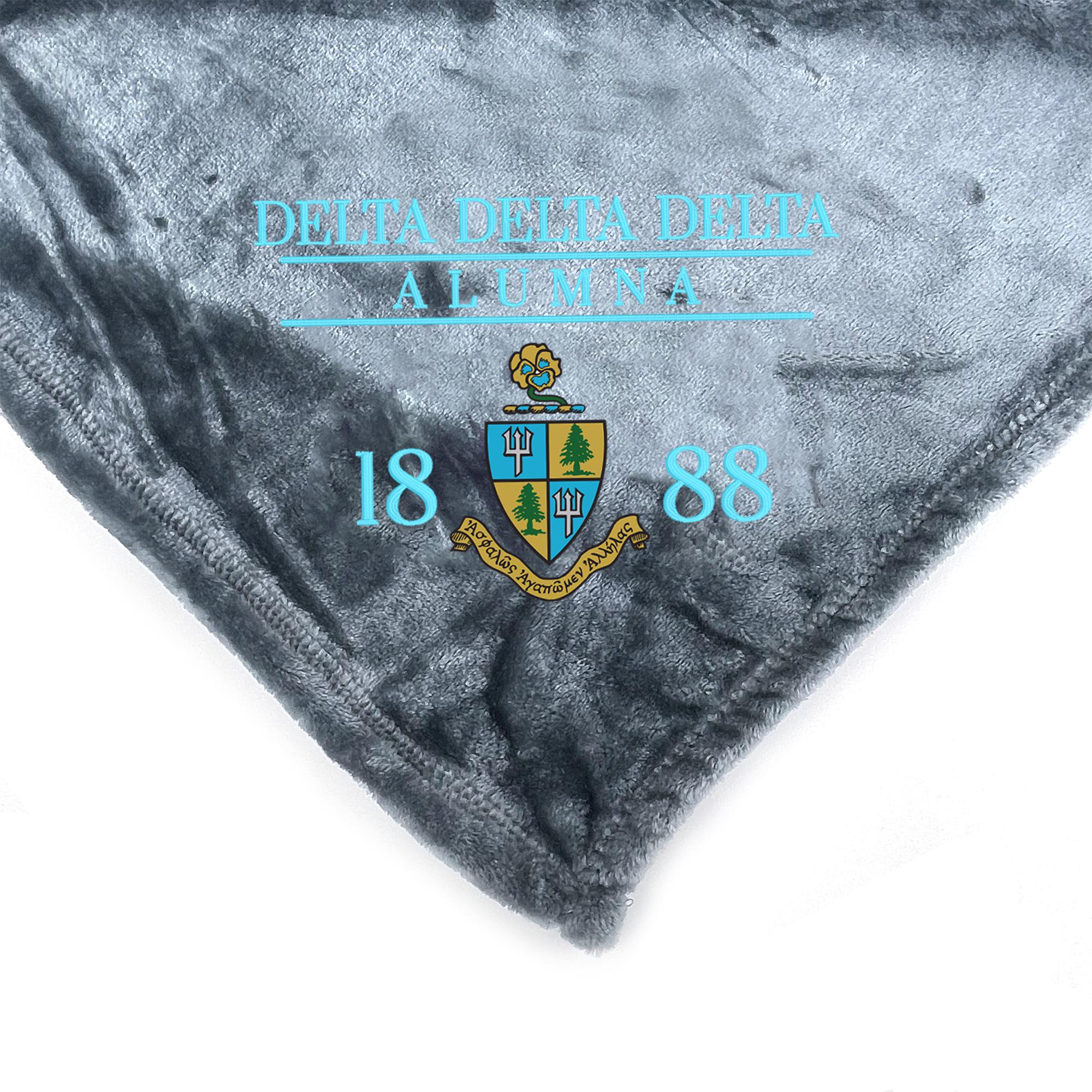 a gray blanket with a blue and gold emblem and text, including the name 'Delta Delta Delta' and the year '1888'.