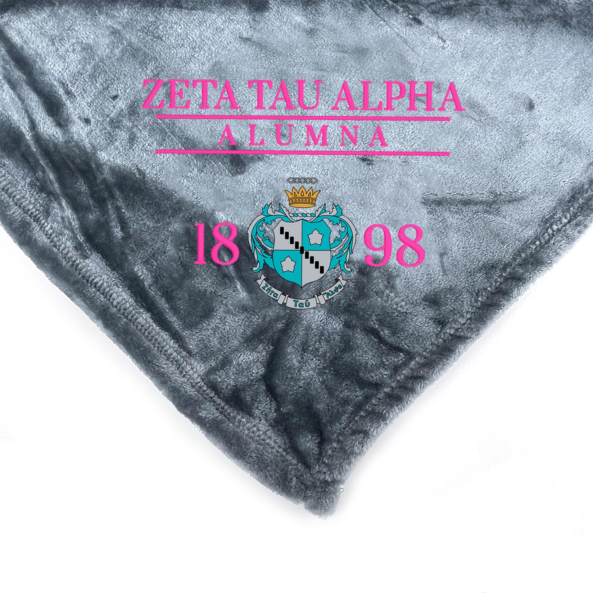 a gray blanket with the text "ZETA TAU ALPHA ALUMNA 18 98" printed on it.