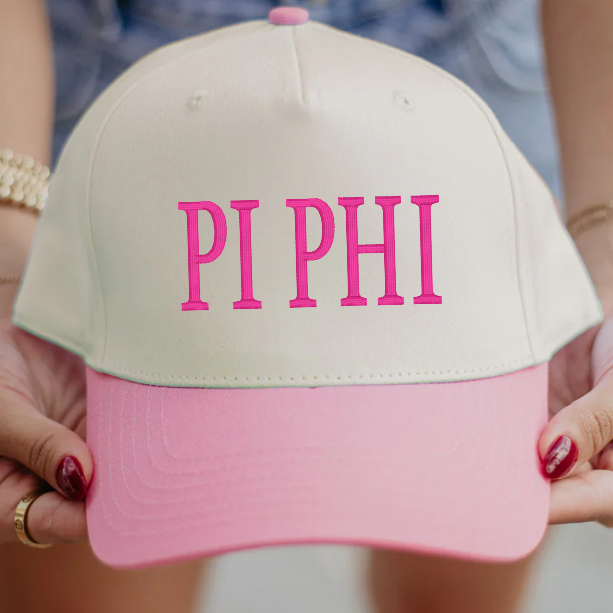 A person is holding a white and pink baseball cap with the text "PI PHI" printed on it.