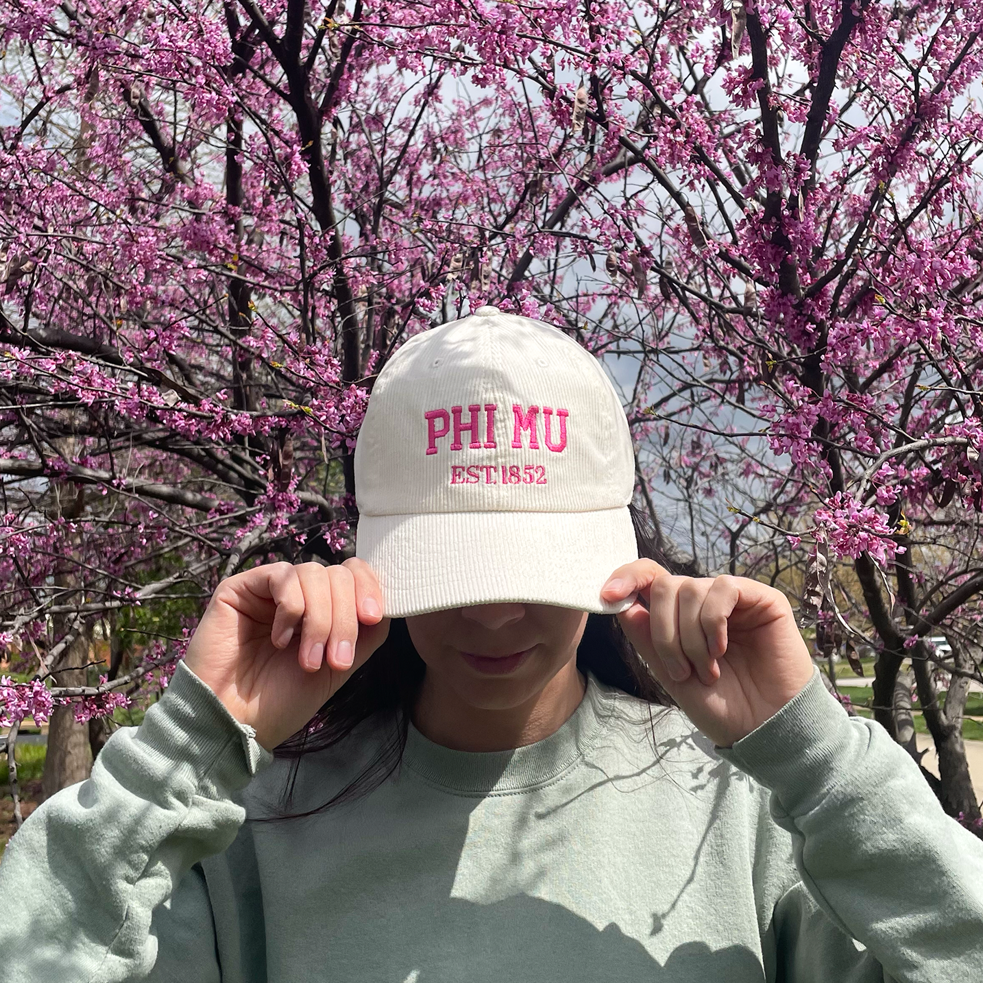 a girl wearing a phi mu hat in front of a tree