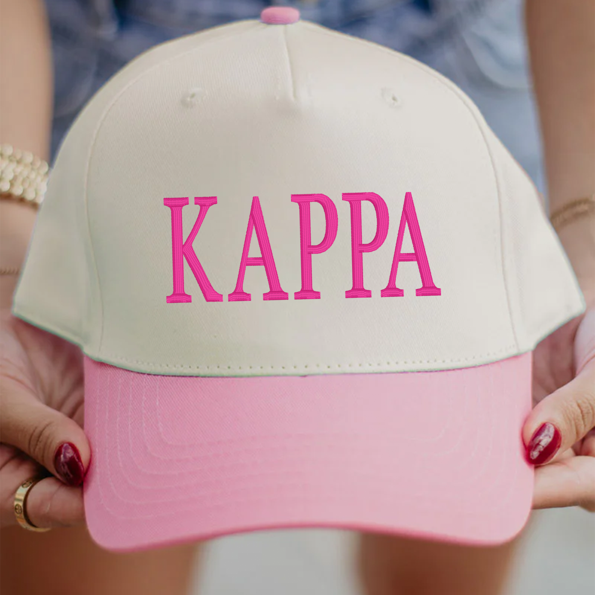 A person is holding a white and pink baseball cap with the word "KAPP" printed on it in pink letters.
