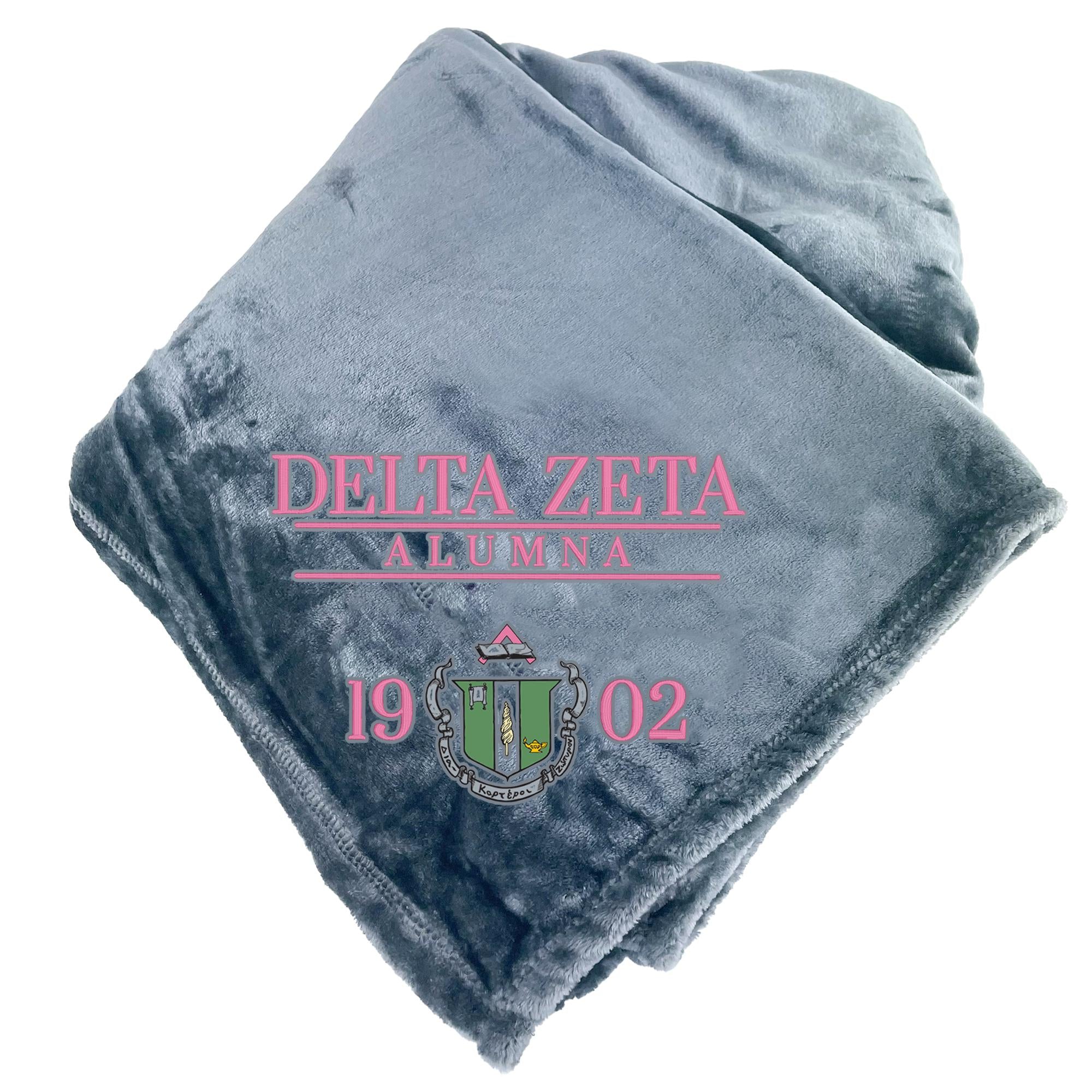 A gray fleece blanket with the text "DELTA ZETA ALUMNA" and a crest design printed on it.