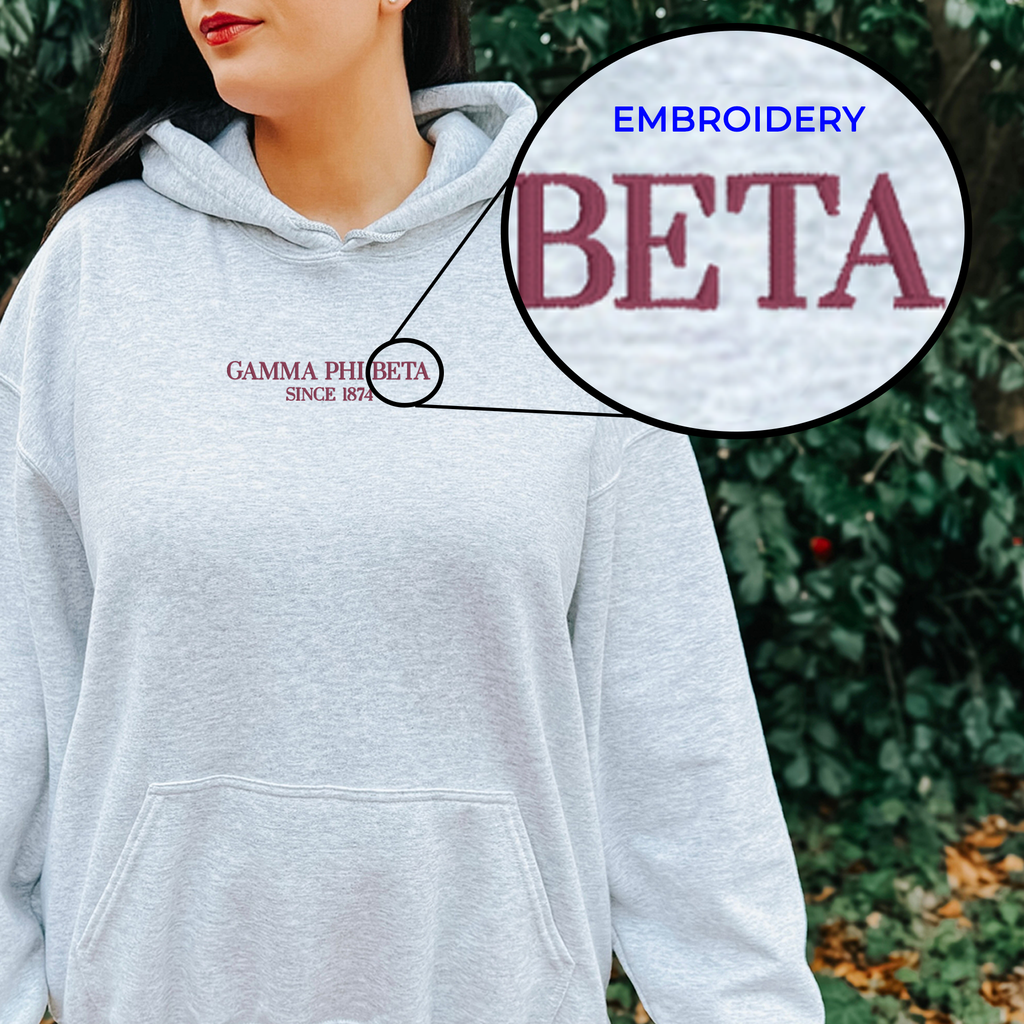 A woman wearing a gray hoodie with the text "Gamma Phi Beta" embroidered on it, standing in front of a natural background.