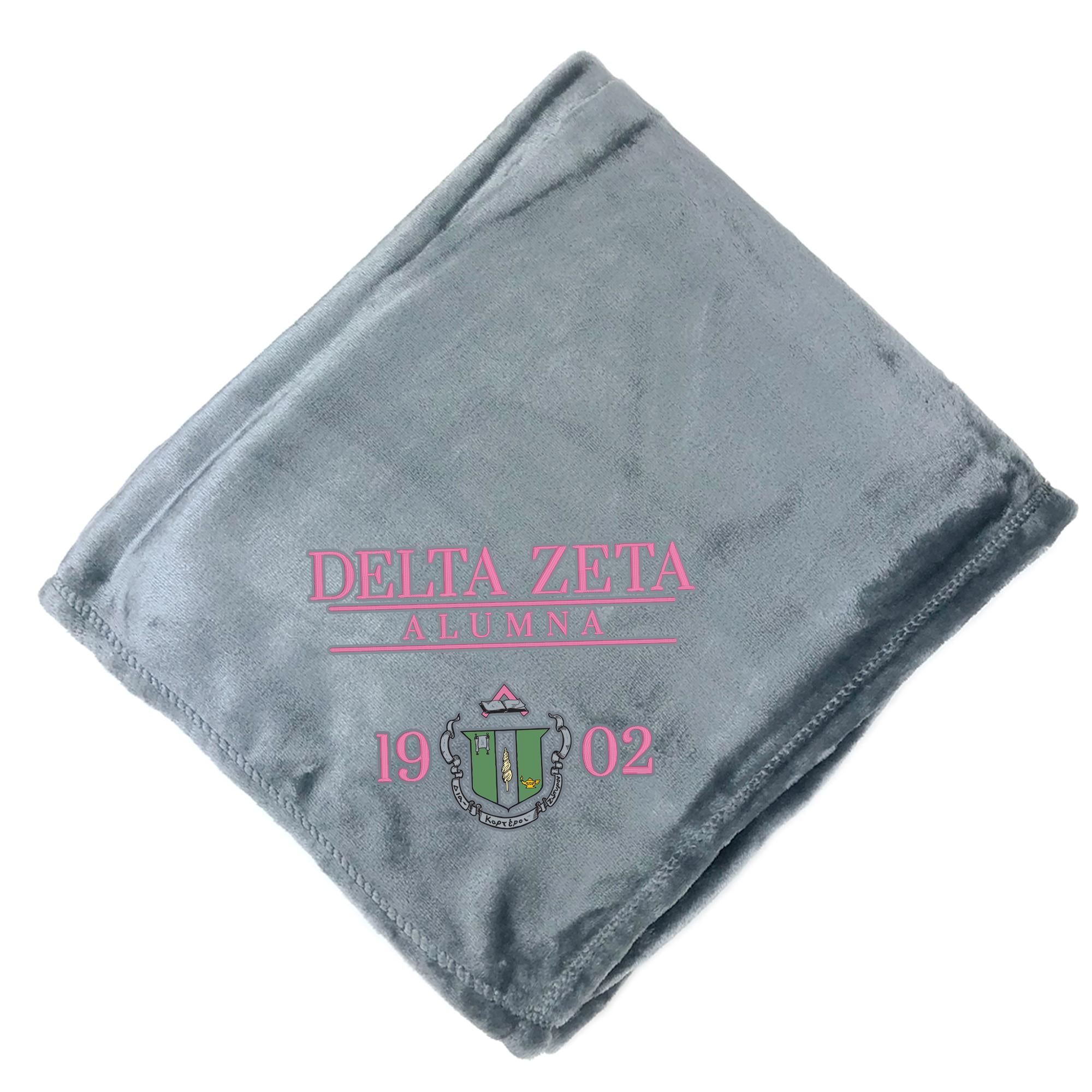 A gray fleece blanket with the text "DELTA ZETA ALUMNA" printed on it, along with a crest and the year "19 2002".