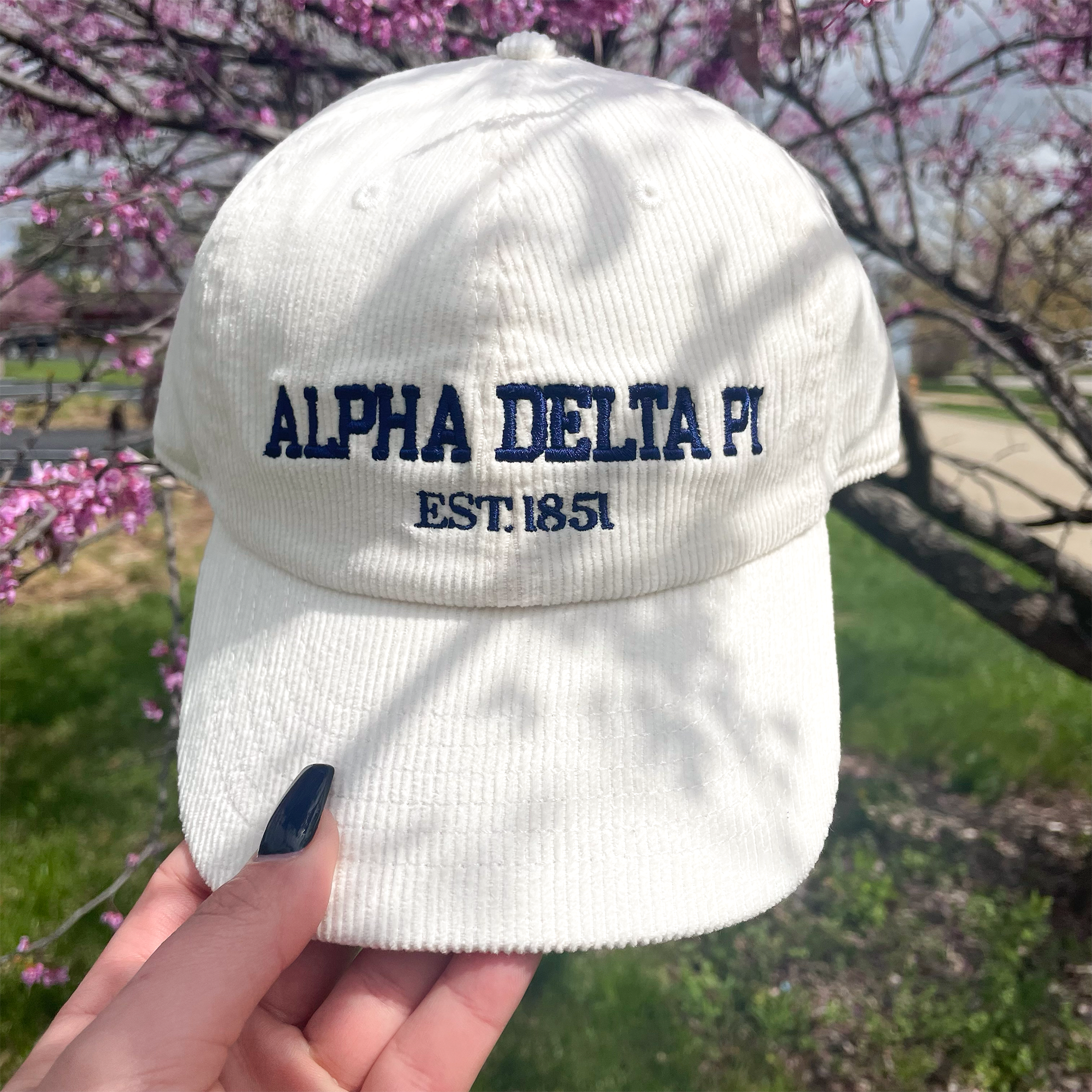 a person holding up a white hat with the words alpha delta on it