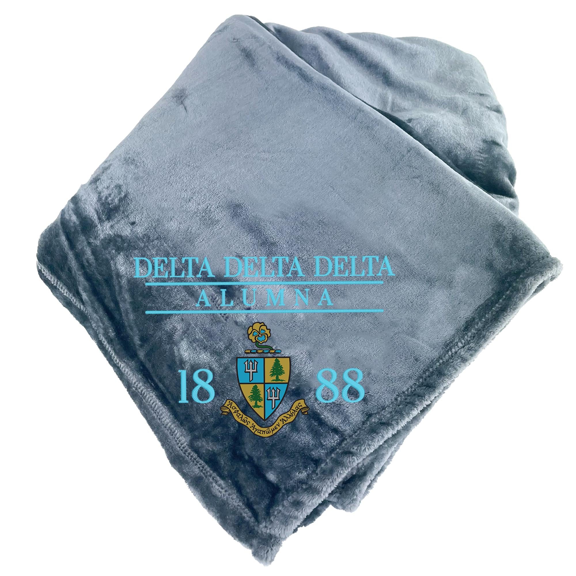 A gray fleece blanket with the text "DELTA DELTA DELTA ALUMNA 18 88" printed on it.