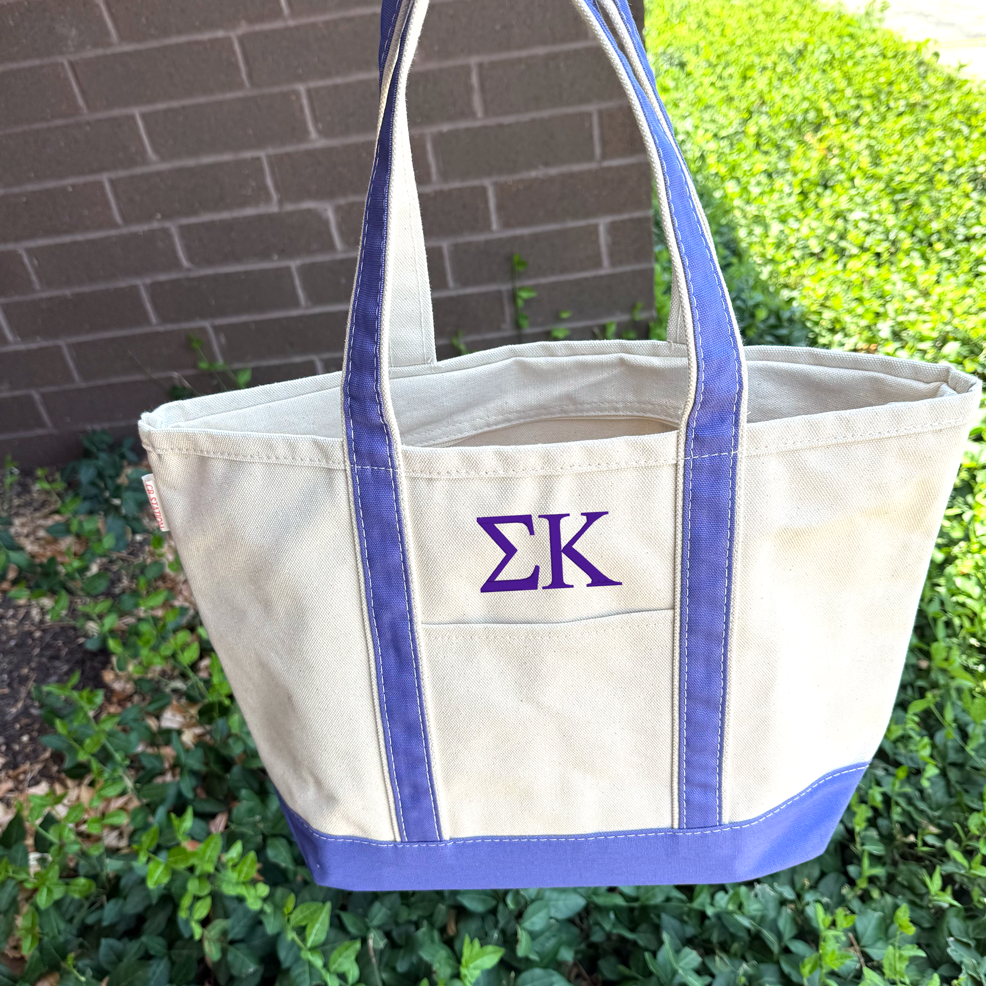 A beige tote bag with blue trim, featuring a purple "ΣΛΕΙ" monogram on the front.