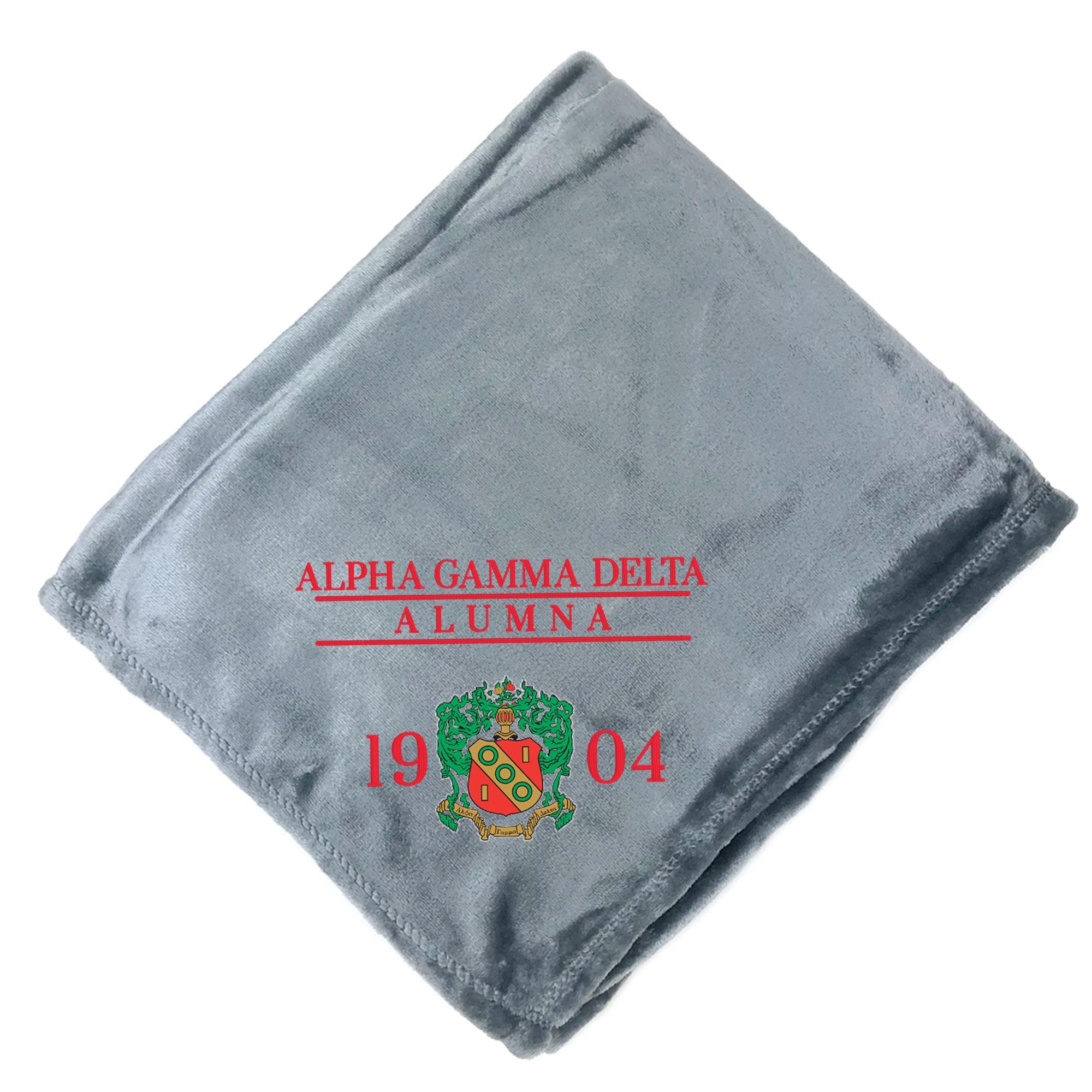 A gray fleece blanket with the text "ALPHA GAMMA DELTA ALUMNA" and the year "1904" printed on it.