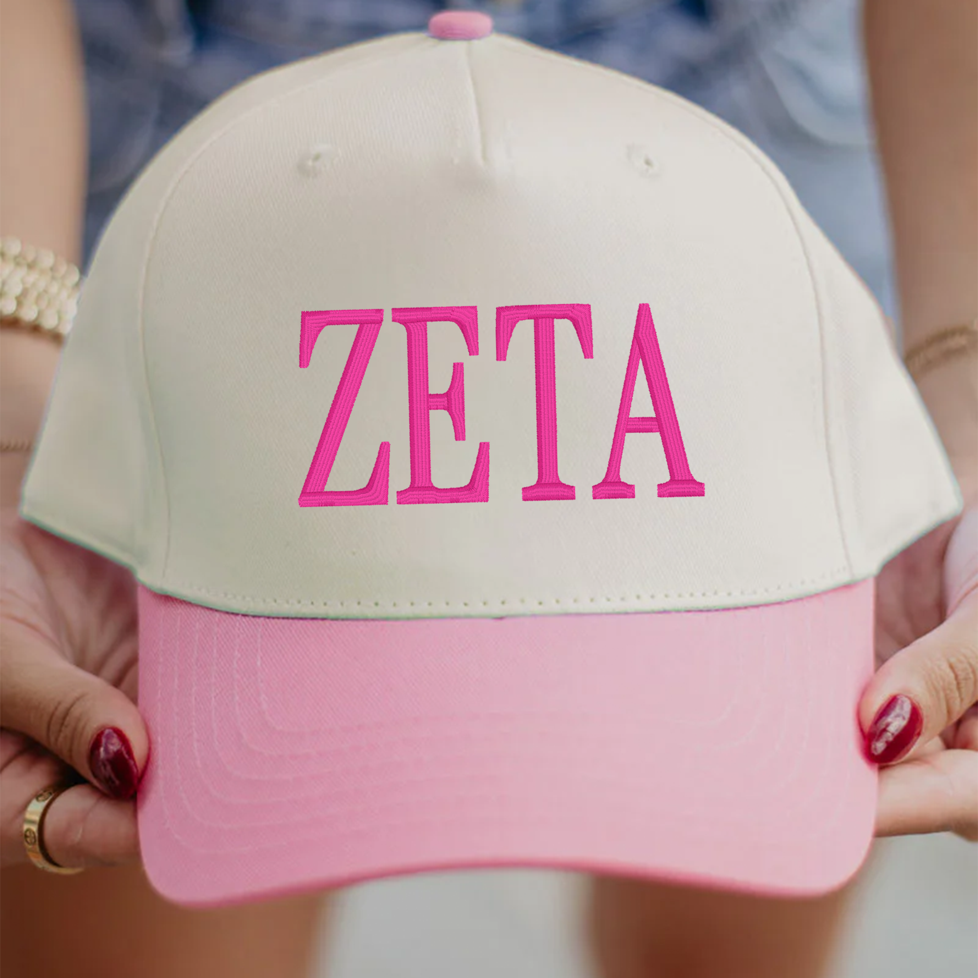 A person is holding a white baseball cap with pink text on it.