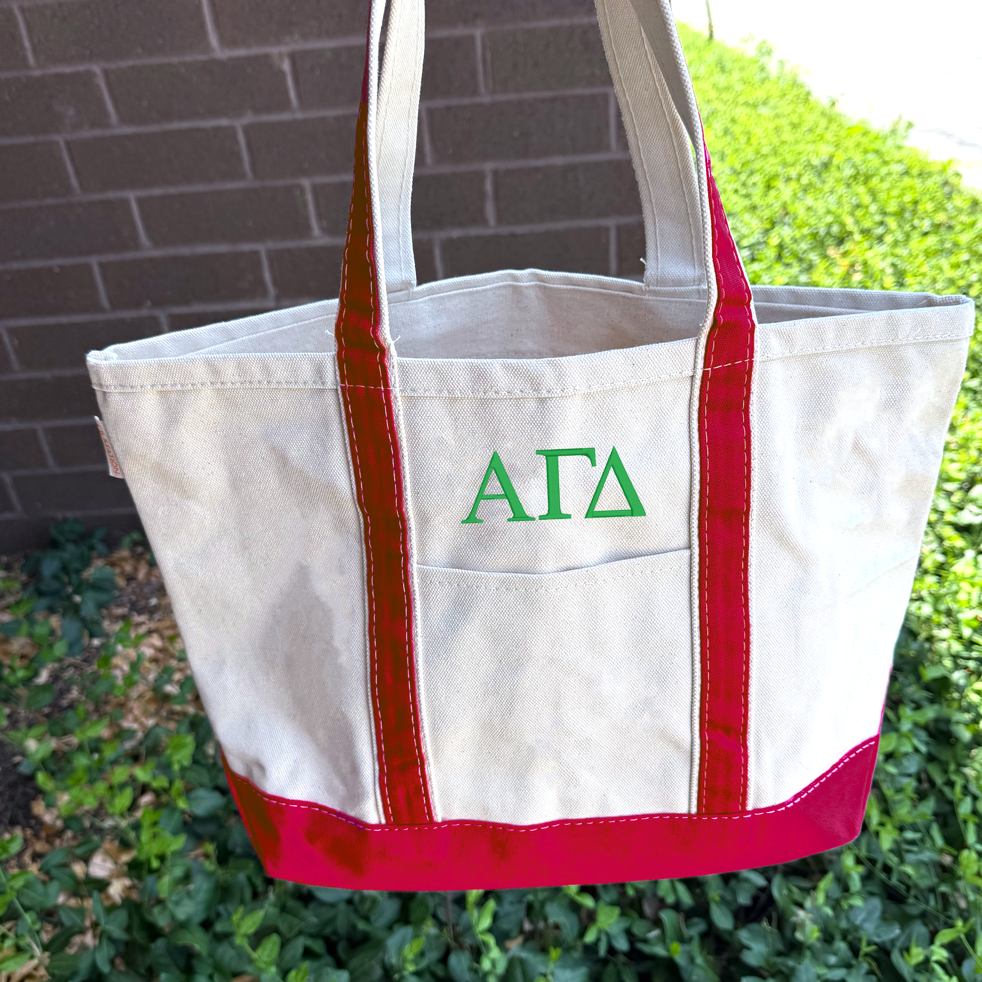 A white tote bag with red trim and the letters 'AFA' printed on it, hanging on a brick wall.